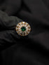Close-up of a gold Ballerina style ring with a round emerald green center stone and sunburst diamond halo.