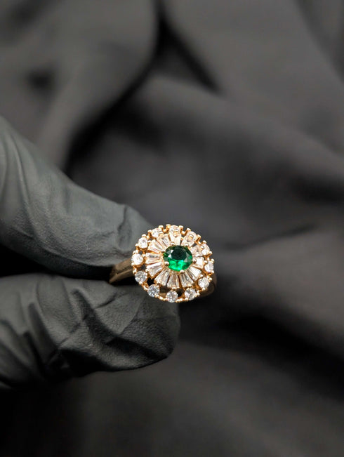Vintage-inspired emerald green cocktail ring with tapered baguette crystal halo held in a gloved hand.