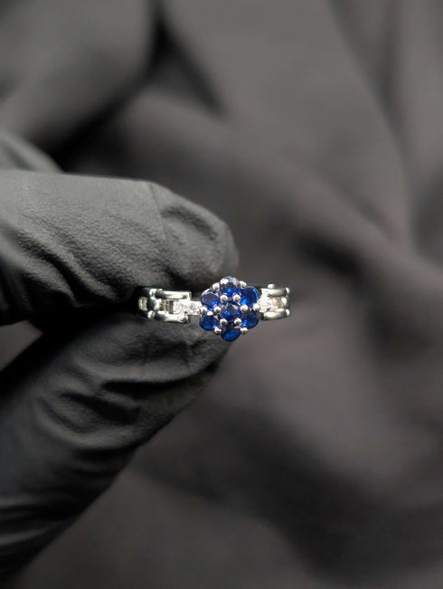 Silver ring featuring a blue sapphire-colored flower cluster center and a unique articulated link band held against a black background.
