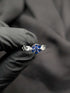 Silver ring featuring a blue sapphire-colored flower cluster center and a unique articulated link band held against a black background.