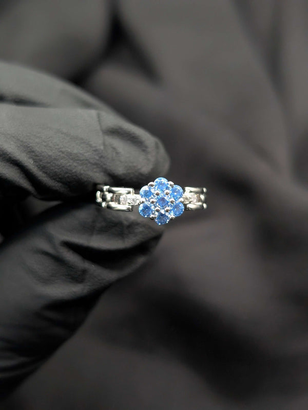 Close-up of a silver ring with a light blue flower-shaped crystal cluster and a unique geometric link-style band.
