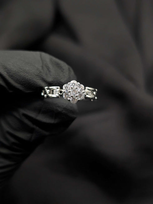A silver-tone ring featuring a brilliant clear floral cluster center and a unique articulated link-style band held in a black gloved hand.