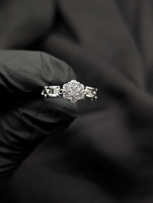 A silver-tone ring featuring a brilliant clear floral cluster center and a unique articulated link-style band held in a black gloved hand.