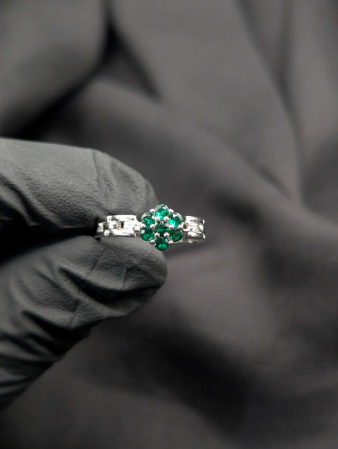 Close-up of a vibrant green emerald-tone flower cluster ring with a polished silver geometric link band.