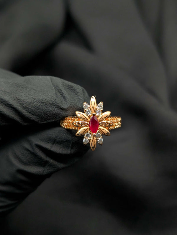 Detailed view of a gold sunburst ring with a red marquise ruby center and clear crystal star accents.