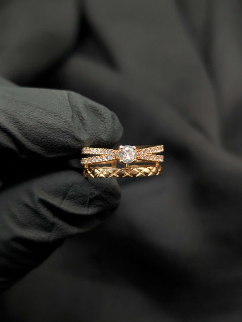 Rose gold statement ring with a stacked 3-tier design featuring a clear solitaire stone and geometric criss-cross bands.