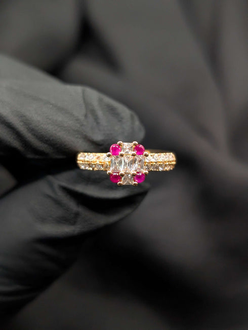 Gold-tone statement ring with a clear rectangular baguette center stone accented by four round ruby-red gems.