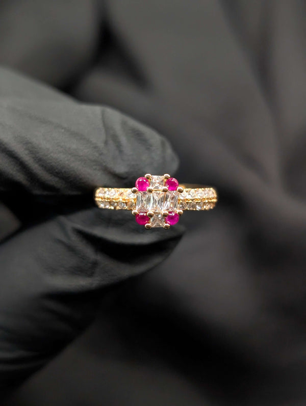 Gold-tone statement ring with a clear rectangular baguette center stone accented by four round ruby-red gems.