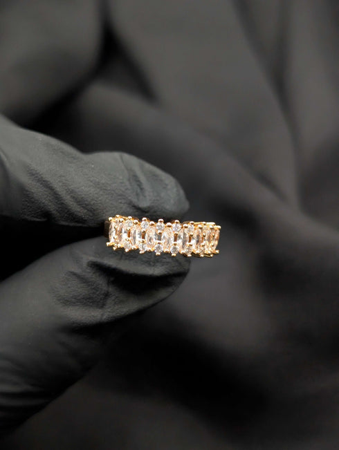 Close-up of a gold-tone eternity band featuring a continuous row of shimmering marquise-cut clear crystals held in a black gloved hand.