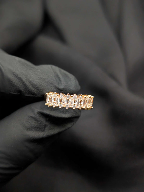 Close-up of a gold-tone eternity band featuring a continuous row of shimmering marquise-cut clear crystals held in a black gloved hand.