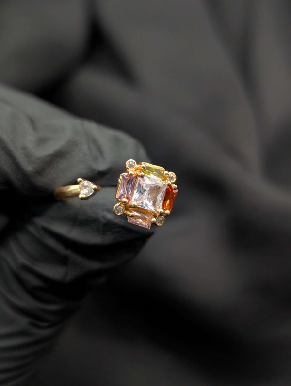 Gold open-ended statement ring featuring a cluster of pastel-colored square and baguette crystals with a clear teardrop accent stone.