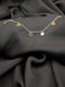 Gold link chain bracelet featuring five circular dangling charms with green, red, black, and white centers laid across a dark grey textured fabric.
