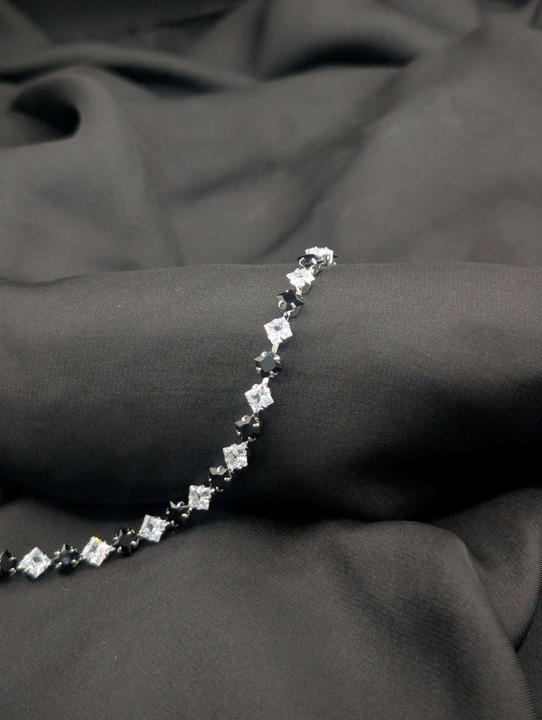 Polished silver-tone tennis bracelet with alternating black onyx and clear white princess-cut crystals on a dark textured background.
