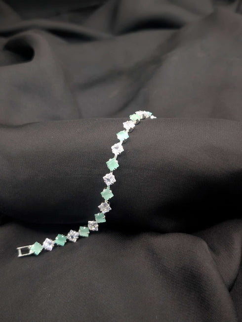 Polished silver-tone tennis bracelet with alternating mint green and clear white princess-cut crystals on a dark textured background.
